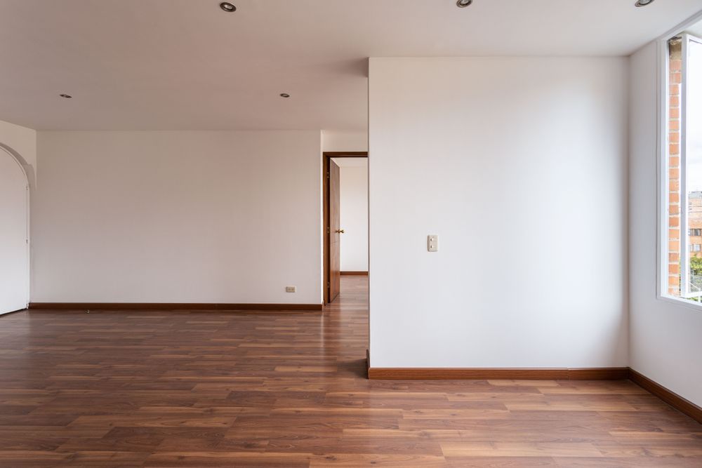 An empty River Heights room with a warm brown hardwood floor running through an open doorway.