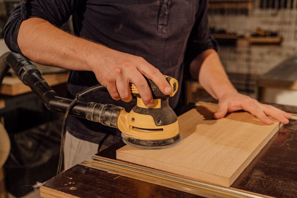 Sanding wood back to bare timber with a dust-extracted orbital sander.